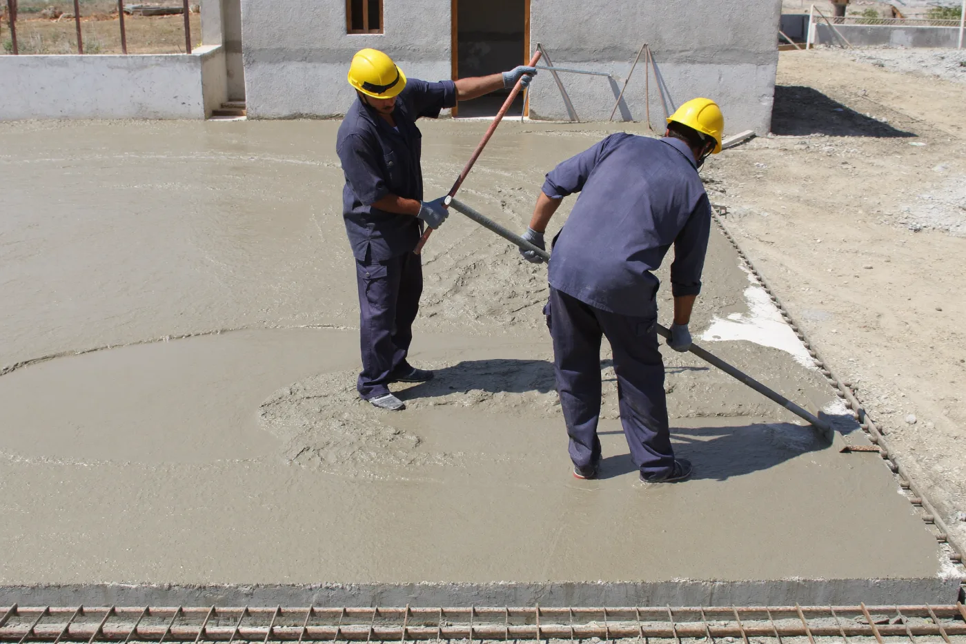 Workers screeding wet concrete level across a villa slab