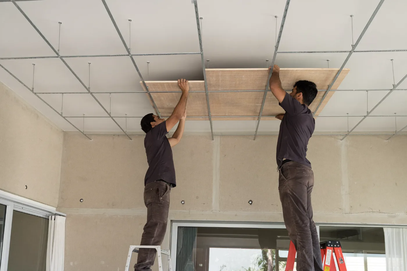 Workers lifting a gypsum board into a suspended ceiling grid